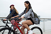 Happy young female friends riding bicycles on bridge