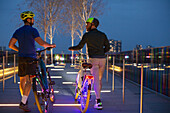 Men walking illuminated bicycles on urban footpath