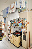 Old wood-fired cooker below shelves and laundry on clothesline in eclectic kitchen