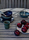 Rote Pflaumen und blaues Keramikgeschirr auf Gartentisch