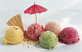 Five scoops of ice cream on a light background, with a wafer and a decorative umbrella