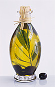 A bottle of olive oil, with an olive branch and some oives