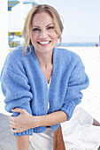 Langhaarige Frau in weißem Sommerkleid und blauer Strickjacke am Strand
