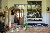 Rustic dining room with wooden table, elongated pendant light and classic painting