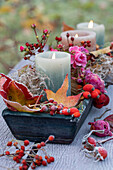 Herbstliche Tischdekoration mit Laub, Kerzen, Rose und Hagebutten