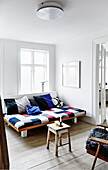 Futon with colorful patchwork cover and wooden stool in a bright living room