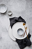 Place setting with white plate, small bowl, golden cutlery, and linen napkin