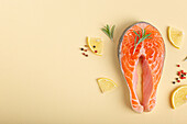 Raw fresh fish salmon steak top view on beige pastel background with rosemary, lemon wedges and spices