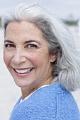 A mature woman with grey hair wearing a blue cardigan on a beach