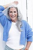 Reife Frau mit grauen Haaren in weißem T-Shirt und blauer Strickjacke
