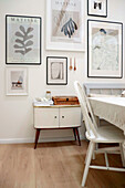 Essbereich mit weißem Stuhl, Vintage-Kommode und gerahmten Kunstwerken an der Wand