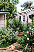 Flower garden with rose bed, pink-painted wooden house in the background