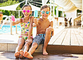 Porträt eines glücklichen kleinen Mädchens und Jungen mit verspiegelten Sonnenbrillen, die ihr Eis am Stiel zeigen