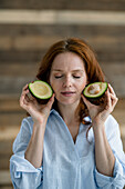 Porträt einer rothaarigen Frau mit geschlossenen Augen, die geschnittene Avocado hält