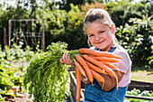 Porträt eines lächelnden Mädchens im Garten, das einen Haufen Karotten hält