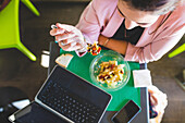 Junge Geschäftsfrau, die gesund zu Mittag isst und Laptop verwendet