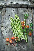 Green asparagus, parsley, tomatoes and mixed peppercorns on wood