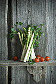 Bundle of green and white asparagus, tomato, parsley and mixed pepper on wood