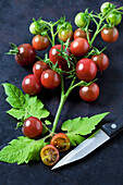 Risp tomatoes 'Black Cherry', leaves and kitchen knife on dark ground