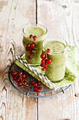 Fresh red currant berries and two glasses of green smoothie