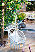 Hanging chair made of rattan with cushions on a wooden terrace in the countryside