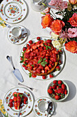 Sommertisch mit Blumenstrauß, Erdbeerkuchen und Kaffeegeschirr