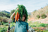 Junge steht im Gemüsegarten und hält ein Bündel Karotten