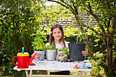 Porträt eines stolzen kleinen Mädchens mit eingetopften Gewürzpflanzen auf dem Tisch im Garten