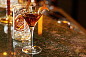 A whisky cocktail in a martini glass, garnished with orange