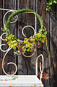 Wreath of fresh flowers on garden bench in front of rustic wooden wall