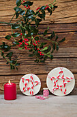 Christmas decorations with red candles, sprigs of holly and round boxes with DIY stars made from straws