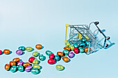 An overturned shopping cart on the ground and spilling colourful Easter eggs on a blue background
