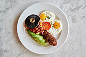 A vegetarian breakfast. Vegetarian sausage, fried eggs, beans, avocado, mushrooms and tomato