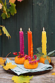 Autumn decoration with colorful candles on mini pumpkins and rose hips