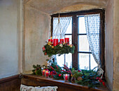 Hängender Adventskranz mit roten Kerzen, darunter weihnachtlich dekorierte Fensterbank
