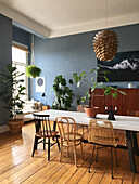 Table with various chairs and houseplants in dining room with blue walls and wooden floorboards