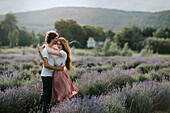 Serene couple standing in lavender field with blossoming flowers and looking away