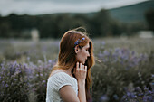 Junge Frau mit Lavendelblüten als Haarschmuck sitzt im Lavendelfeld