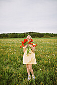 Content female in dress standing with bunch of red tulip flowers in meadow in summer with closed eyes