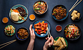 Set of Chinese dishes on table, female hands holding chopsticks