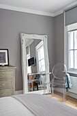 Großer Spiegel mit Holzrahmen an graue Wand gelehnt und Designerstuhl im Schlafzimmer