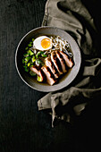 Asian style soup with rice noodles, grilled duck breast and boiled egg in ceramic bowl