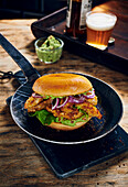 A crispy chicken burger with red onions and avocado cream in serving pan