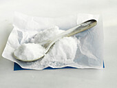 A heap of table salt with a spoon on paper