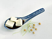 Asiatischer Löffel mit Tofuwürfeln und Sojasauce, daneben einige Sojabohnen