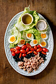 Layered nicoise salad with canned tuna fish, olives and eggs, served with olive oil dressing and sea salt