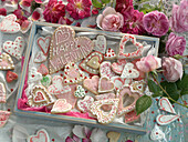 Herzförmiges Gebäck aus Mürbeteig mit Zuckerdeko und Baiser, umgeben von Rosen