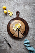 A sliced lemon cake on a wood cutting board with fresh lemons