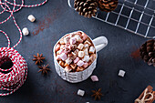 Ceramic mug with sweet cocoa with marshmallows near fir cones and rope for tying Xmas gifts