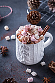 Ceramic mug with sweet cocoa with marshmallows near fir cones and rope for tying Xmas gifts